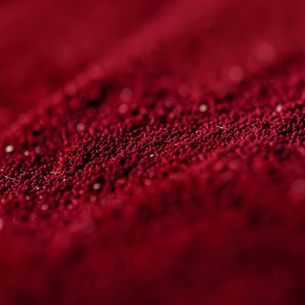 close-up of dark red textured fabric with faint gold thread pattern, moody and warm
